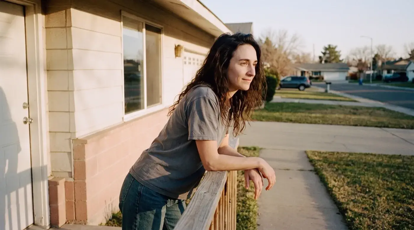 After CreditHound: the same woman at the same house, leaning on her own porch rail in warm evening light, relaxed